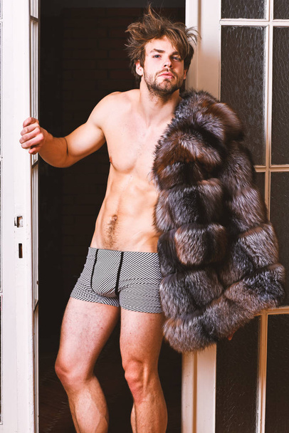 Bachelor rich lover. Guy attractive posing fur coat on naked body. Richness and luxury concept. Luxury lifestyle and wellbeing. Luxury status symbol. Sexy macho tousled hair coming out bedroom door - Photo, image