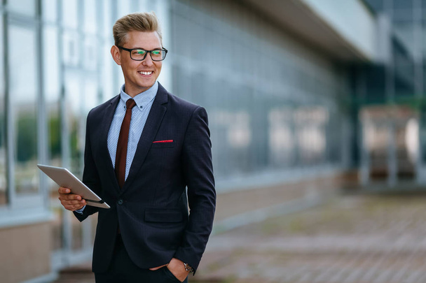 Elegant smiling young businessman using his PC tablet. Portrait of a Male executive manager in trendy clothes with tablet pc in front of office building. Modern technology concept - Photo, image