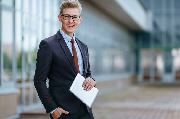 Happy smiling businessman with digital tablet. Portrait of a Male executive manager in trendy clothes with tablet PC in hand on background of office building. Modern technology concept - Foto, afbeelding