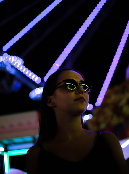 Beautiful girl in neon lights at night in an amusement park. - 写真・画像