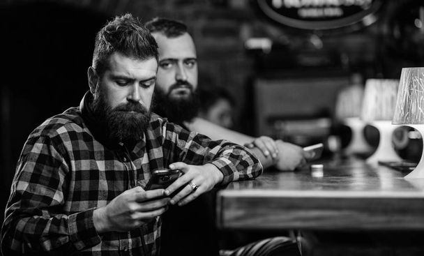 Order drinks at bar counter. Men with smartphone relaxing at bar. Mobile dependence concept. Mobile phone always with me. Friday relaxation in bar. Hipster bearded man spend leisure at bar counter - Fotoğraf, Görsel