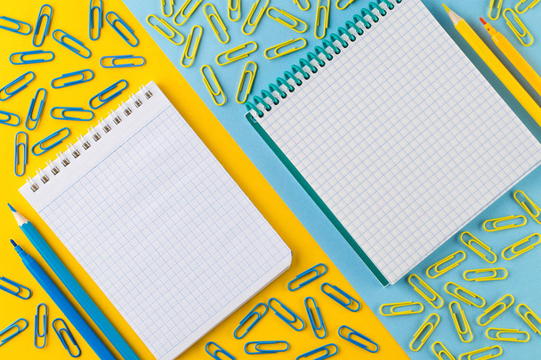 Συνδετήρες χαρτιού και σημειωματάριο σε έντονο κίτρινο και μπλε χαρτί φόντου. - Φωτογραφία, εικόνα