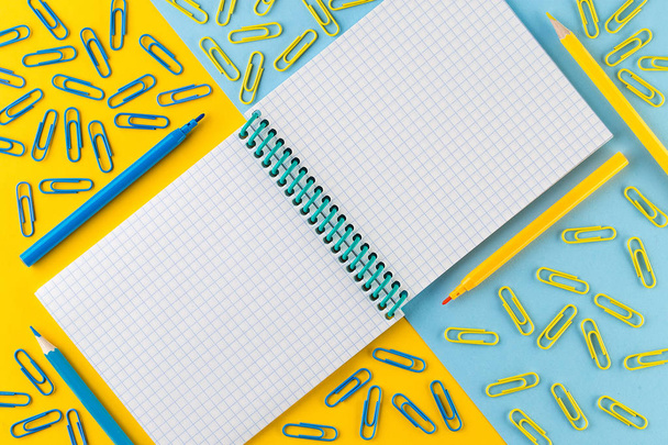 Paper clips and Notepad on bright yellow and blue paper background - Fotografie, Obrázek