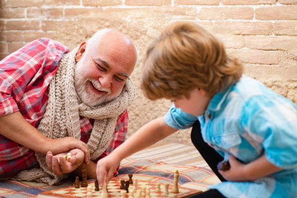 Cute little boy playing chess. Childhood. Cute little boy playing chess. Generations. Handsome grandpa and grandson are playing chess while spending time together at home. - Foto, Imagem