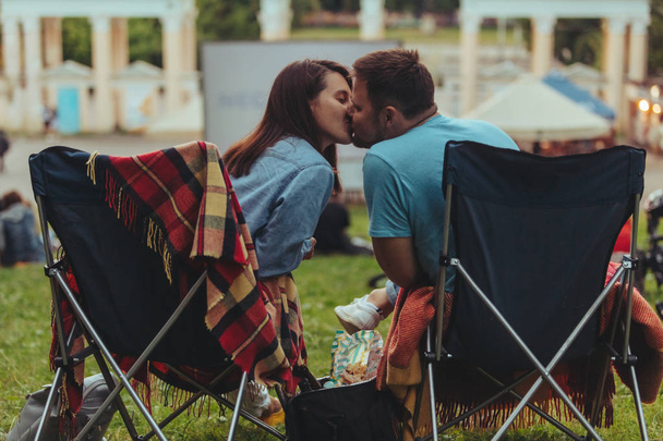 屋外映画館で屋外で映画を見て、都市公園のキャンプチェアに座っているカップル - 写真・画像