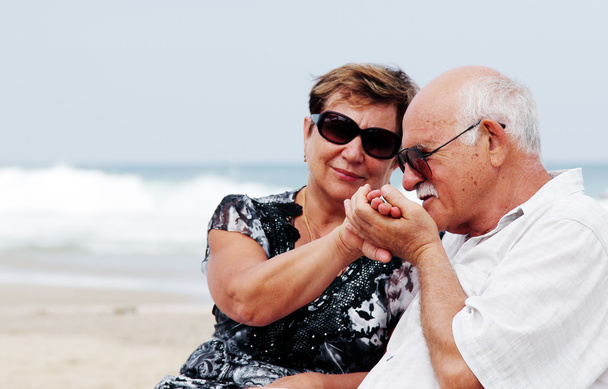 Porträt eines glücklichen Senioren-Paares, das zusammen am Strand sitzt - Foto, Bild