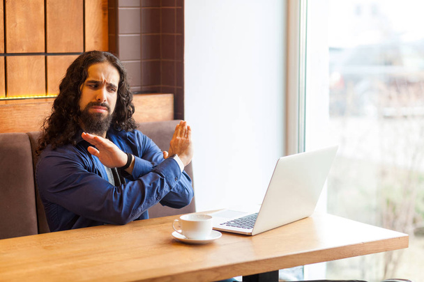 angry handsome young adult man freelancer in casual style sitting in cafe and talking with friend in laptop while showing stop gesture with hands  - Foto, Bild