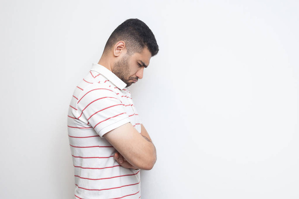 side view of sad depressed bearded young man in striped t-shirt holding his head down and feeling bad isolated on white background - Foto, immagini