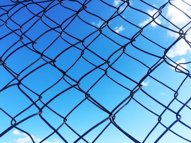 Fémháló kerítés, mögötte egy ragyogó kék eget. Közeli. - Fotó, kép
