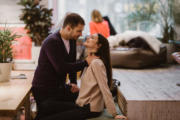 Happy loving guy puts his hands at the girls shoulders sitting at the table in the cafe and looks at her - Фото, зображення