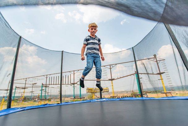 El niño salta en un trampolín en un parque de atracciones, realizando varias acrobacias
. - Foto, Imagen