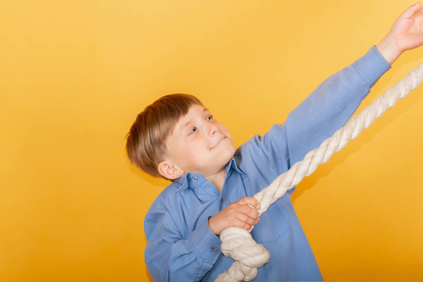 De jongen strekt zich uit op een touw op een gele achtergrond, het concept van het behalen van succes. - Foto, afbeelding