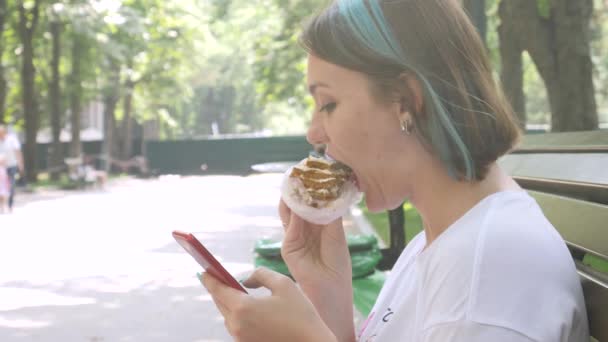 Encantadora mujer lee el mensaje en el teléfono inteligente y comer pastel
 - Imágenes, Vídeo
