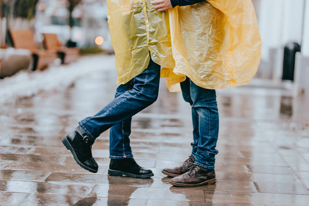 Piernas de chico y chica en jeans y impermeables amarillos en la calle bajo la lluvia
 - Foto, Imagen