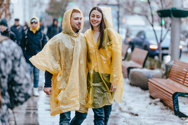 Guy y su novia vestidos con impermeables amarillos están caminando en la calle bajo la lluvia
 - Foto, imagen