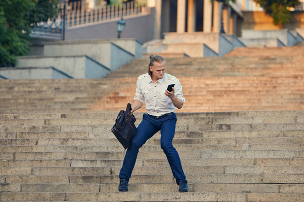 Crazy young businessman dancing on the street with bag. Celebrating victory. Flexibility and grace in business - Fotografie, Obrázek