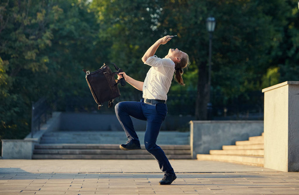 Crazy young businessman dancing on the street with bag. Celebrating victory. Flexibility and grace in business - Photo, Image