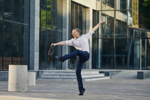 Verrückter junger Geschäftsmann, der mit Tasche auf der Straße tanzt. Sieg feiern. Flexibilität und Anmut in der Wirtschaft - Foto, Bild