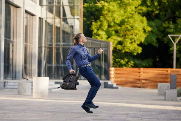 Crazy young businessman dancing on the street with bag. Celebrating victory. Flexibility and grace in business - Photo, Image