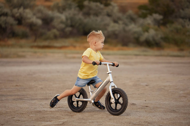 little toddler boy riding balance bike at sunset beach - Fotó, kép
