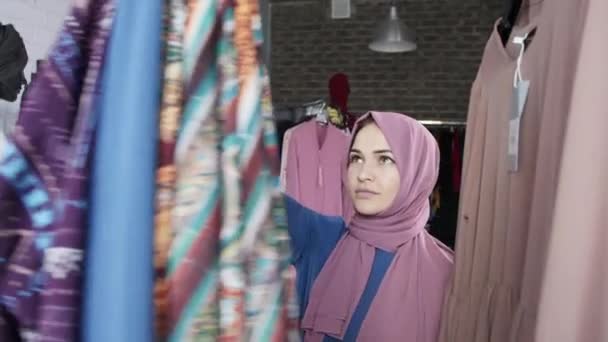 Μια νεαρή μουσουλμανική γυναίκα που επιλέγει ρούχα στο κατάστημα - Πλάνα, βίντεο