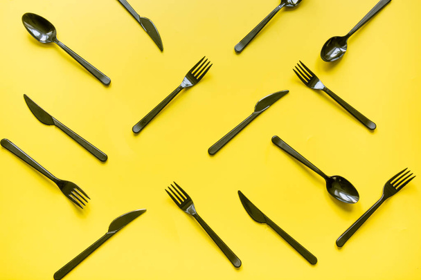 Disposable picnic black knife and forks in diagonal on yellow. Top view. Flat lay. - 写真・画像