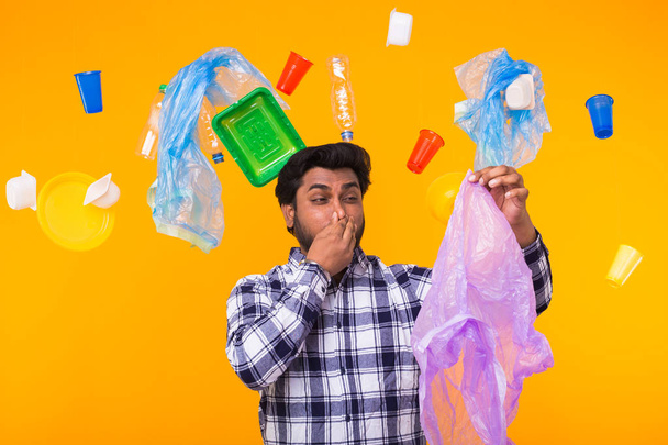 Wereldmilieudag, kunststof recycling probleem en milieuramp concept-boos Indiase man sluiten neus omdat hij wordt gevoeld slechte geur van vuilnis op gele achtergrond. - Foto, afbeelding