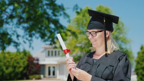 Retrato de una mujer con manto y gorra de graduación, con un diploma en la mano sobre el fondo de su casa
 - Imágenes, Vídeo
