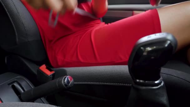 Mulher de vestido vermelho que fixa o cinto de segurança do carro enquanto está sentado dentro do veículo antes de dirigir
 - Filmagem, Vídeo