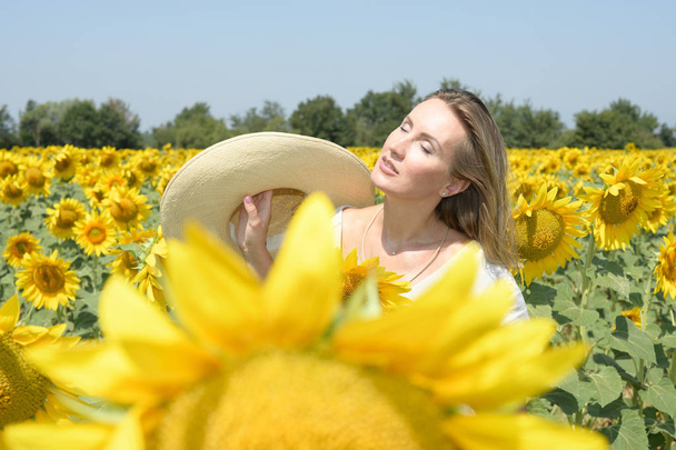 Jovem em um campo de girassol com um chapéu na mão toma um banho de sol
 - Foto, Imagem