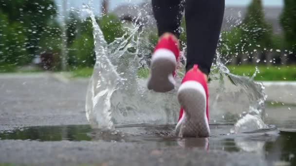 Legs of a runner in sneakers. Sports woman jogging outdoors, stepping into muddy puddle. Single runner running in rain, making splash - Footage, Video