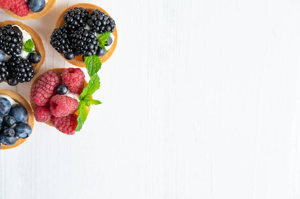 Background with tartlets. Berry tartlets with space for copy space. Cupcakes with raspberries, blueberries and blueberries on a white wooden background. Advertising banner with sweets. View from above - Photo, Image