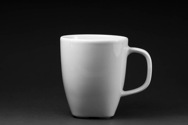 Modèle d'une tasse en porcelaine blanche isolée sur un fond noir qui s'étend verticalement
. - Photo, image