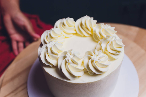 Кондитер украшен ягодами бисквитный торт с белым кремом. Торт стоит на деревянном столе. Концепция домашней выпечки, приготовления тортов
. - Фото, изображение