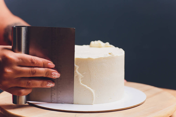 Frauenhände backen Kekskuchen mit weißer Sahne mit einem Kochspachtel. - Foto, Bild