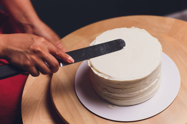 womens hands making biscuit cake with white cream using a cooking spatula. - Foto, afbeelding