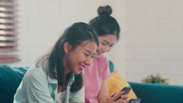 Young Lesbian lgbtq Asian women couple using mobile phone at home. Asian lover female happy relax fun using technology check social media in internet together while lying sofa in living room concept. - Video, Çekim