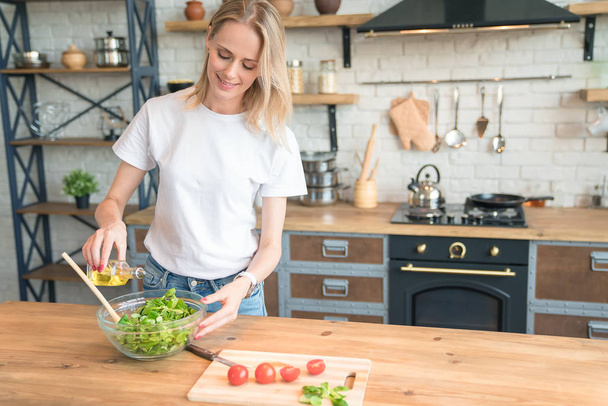 beautiful young smiling woman making salad in the kitchen. Healthy food. vegetable salad. Diet. Healthy lifestyle. cooking at home. Wearing white shirt and jeans. - Photo, Image