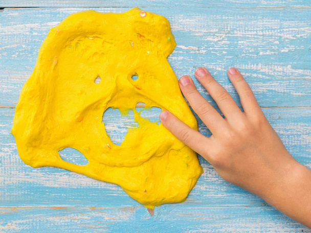 Το παιδί τεντώνει το δεξί του χέρι από την κίτρινη λάσπη σε ένα μπλε τραπέζι. - Φωτογραφία, εικόνα