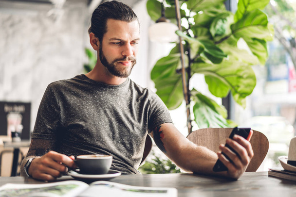 Handsome bearded hipster man use smartphone with coffee at table - Photo, image