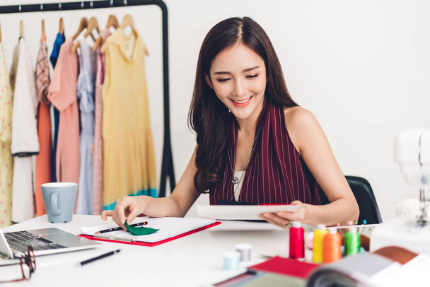 Посміхаючись Азії жінка моди дизайнер працює з ноутбуком комп'ютера
 - Фото, зображення