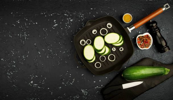 Fresh zucchini in a frying pan with seasoning on a dark table. View from above. Copy space - Photo, image