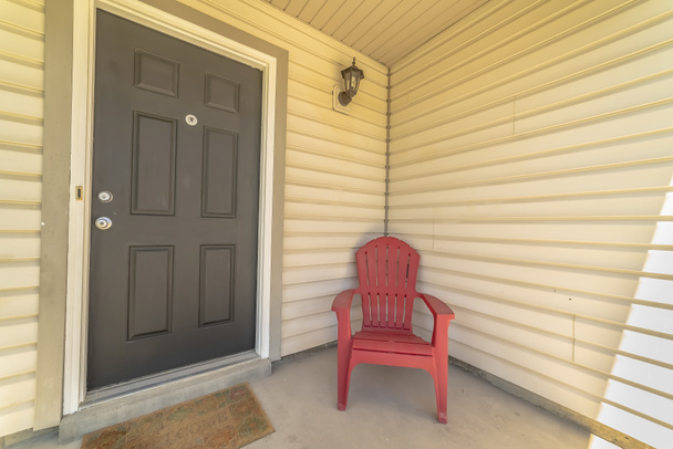 Wejście do domu z szarymi drzwiami i czerwonym drewnianym krzesłem na ganku - Zdjęcie, obraz