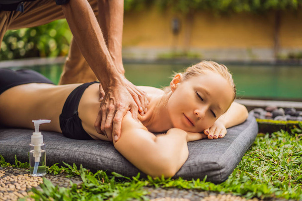 Молода жінка відпочиває на вулиці в оздоровчому спа-центрі біля басейну, маючи масаж
 - Фото, зображення