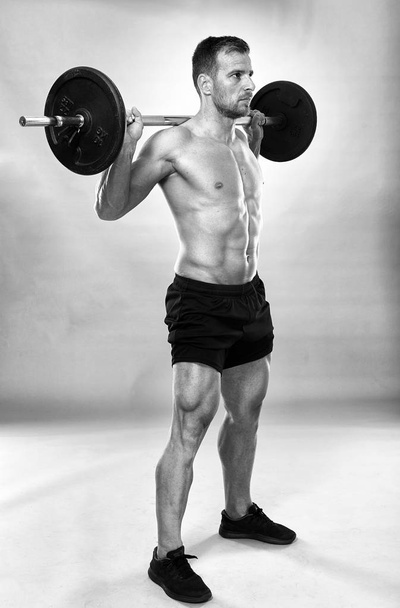 Man doing squats with barbell on neck back, studio shot - Fotó, kép