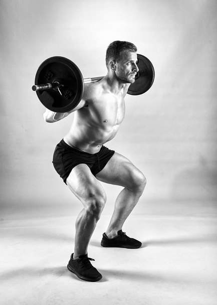 Man doing squats with barbell on neck back, studio shot - Photo, Image