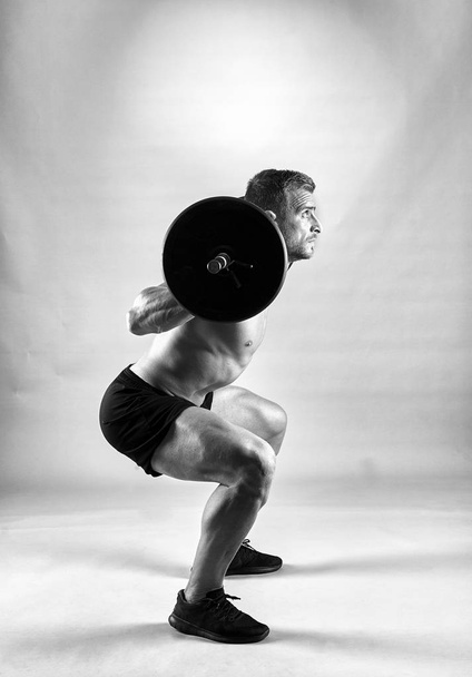 Man doing squats with barbell on neck back, studio shot - 写真・画像