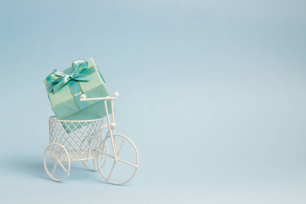 A toy bike carries a gift. The idea for a postcard. Blue background. Minimalism. - Foto, imagen