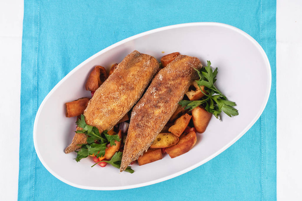 Grilled fish steak is served in batter with braised and roasted potato wedges. Mediterranean cuisine, European dish - Φωτογραφία, εικόνα