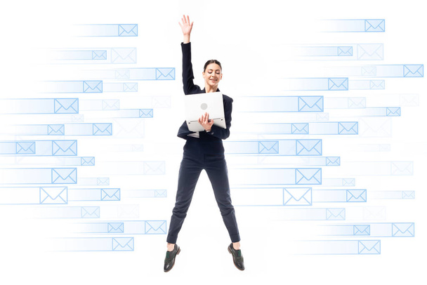 sonriente mujer de negocios utilizando el ordenador portátil mientras salta sobre el fondo con iconos de correo electrónico aislados en blanco
 - Foto, Imagen